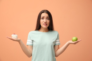 Photo of Woman choosing between apple and cake on orange background