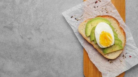 Delicious sandwich with boiled egg and pieces of avocado on gray table, top view. Space for text