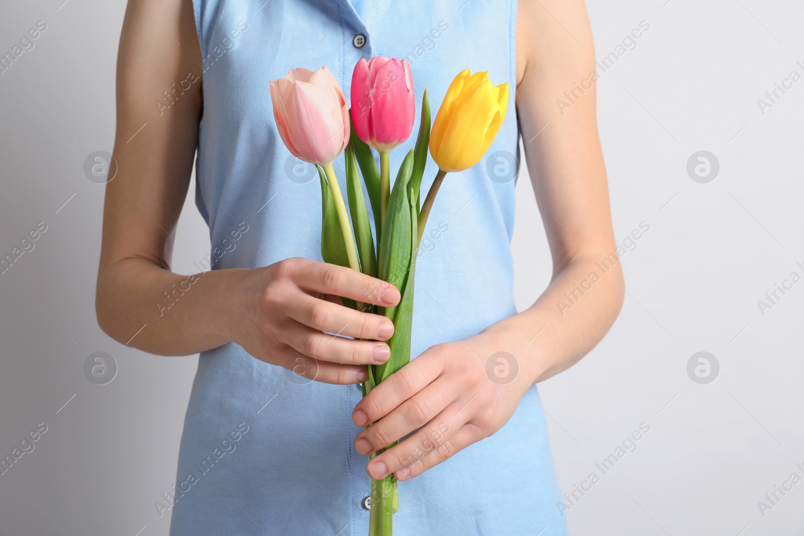 Photo of Girl holding beautiful spring tulips on light background, closeup. International Women's Day