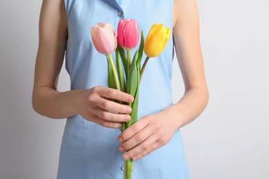 Girl holding beautiful spring tulips on light background, closeup. International Women's Day