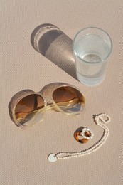 Stylish sunglasses, glass of water and jewelry on grey surface, above view