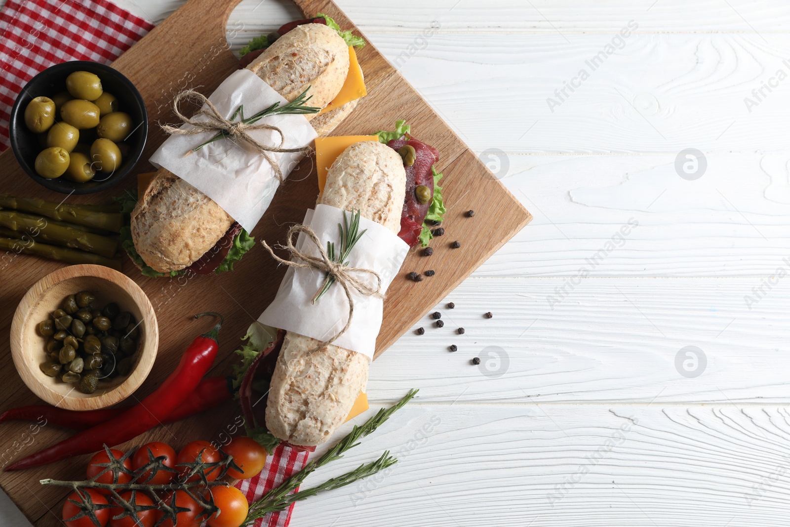 Photo of Delicious sandwiches with bresaola, cheese and other products on white wooden table, flat lay. Space for text