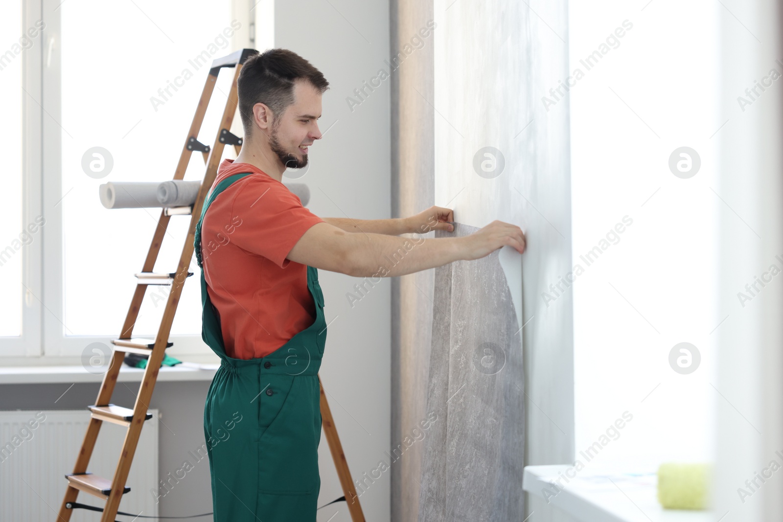 Photo of Man hanging stylish gray wallpaper in room