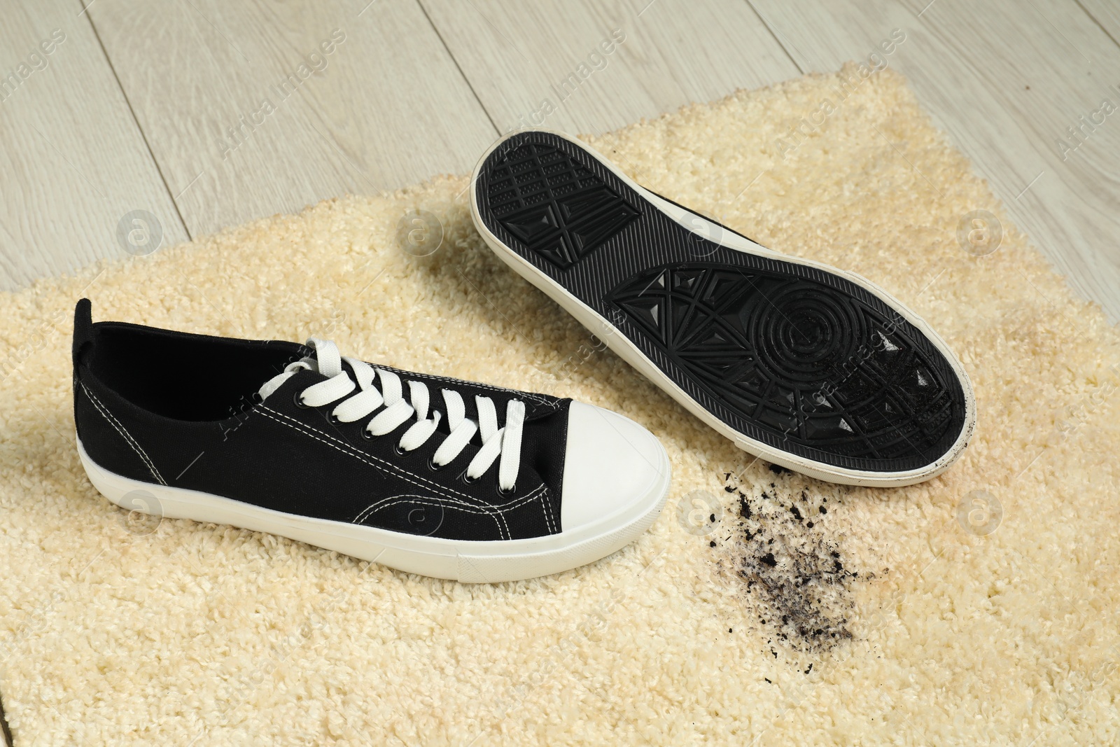 Photo of Black sneakers and mud on beige carpet, closeup