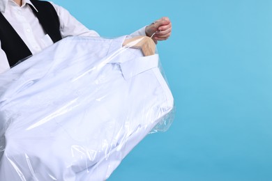 Dry-cleaning service. Woman holding shirt in plastic bag on light blue background, closeup. Space for text