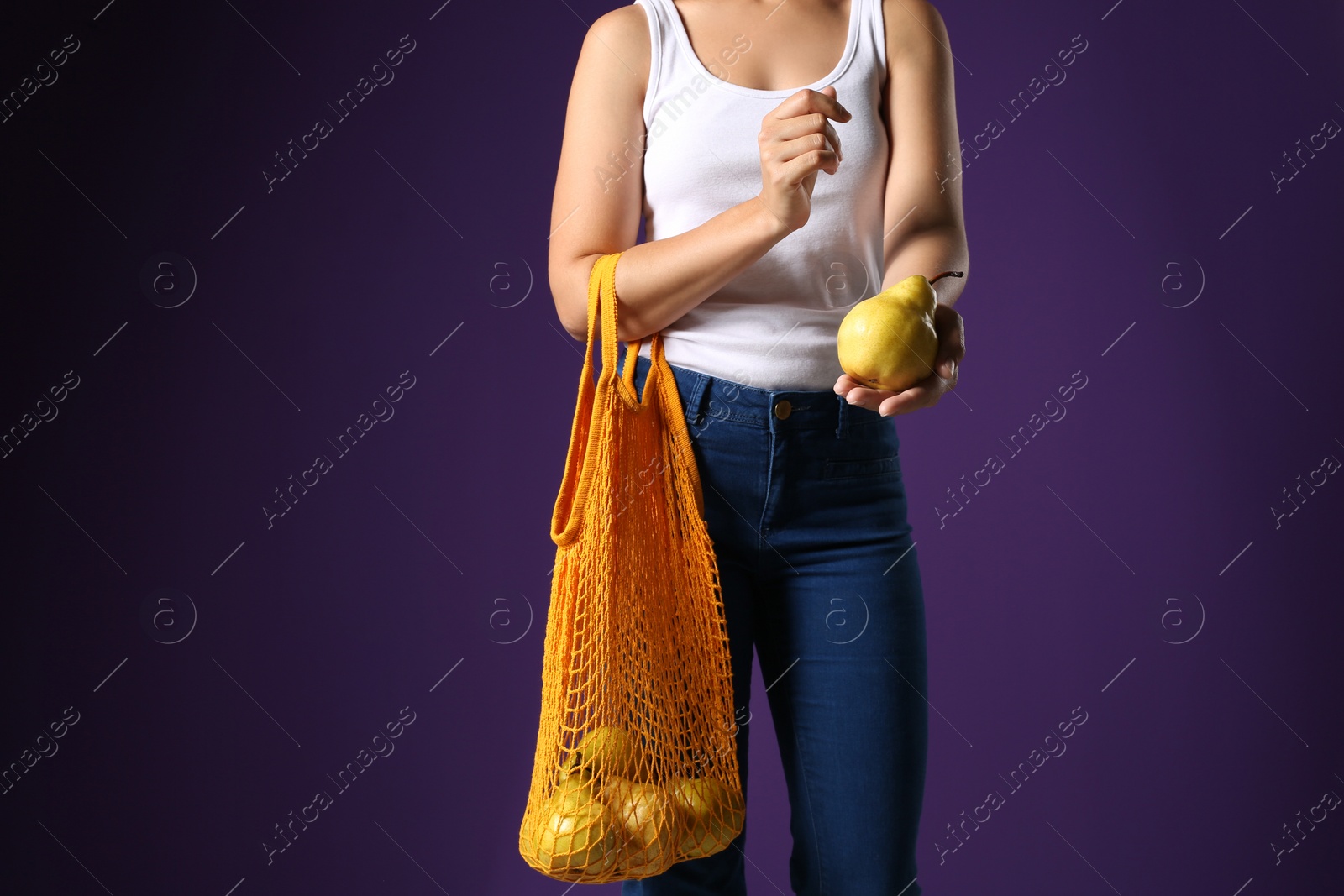 Photo of Woman holding net bag with fresh ripe pears on purple background, closeup