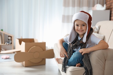 Photo of Cute little boy in pilot hat and blurred cardboard airplane on background. Space for text