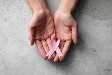 Photo of Woman holding pink ribbon at grey table, top view. Breast cancer awareness concept