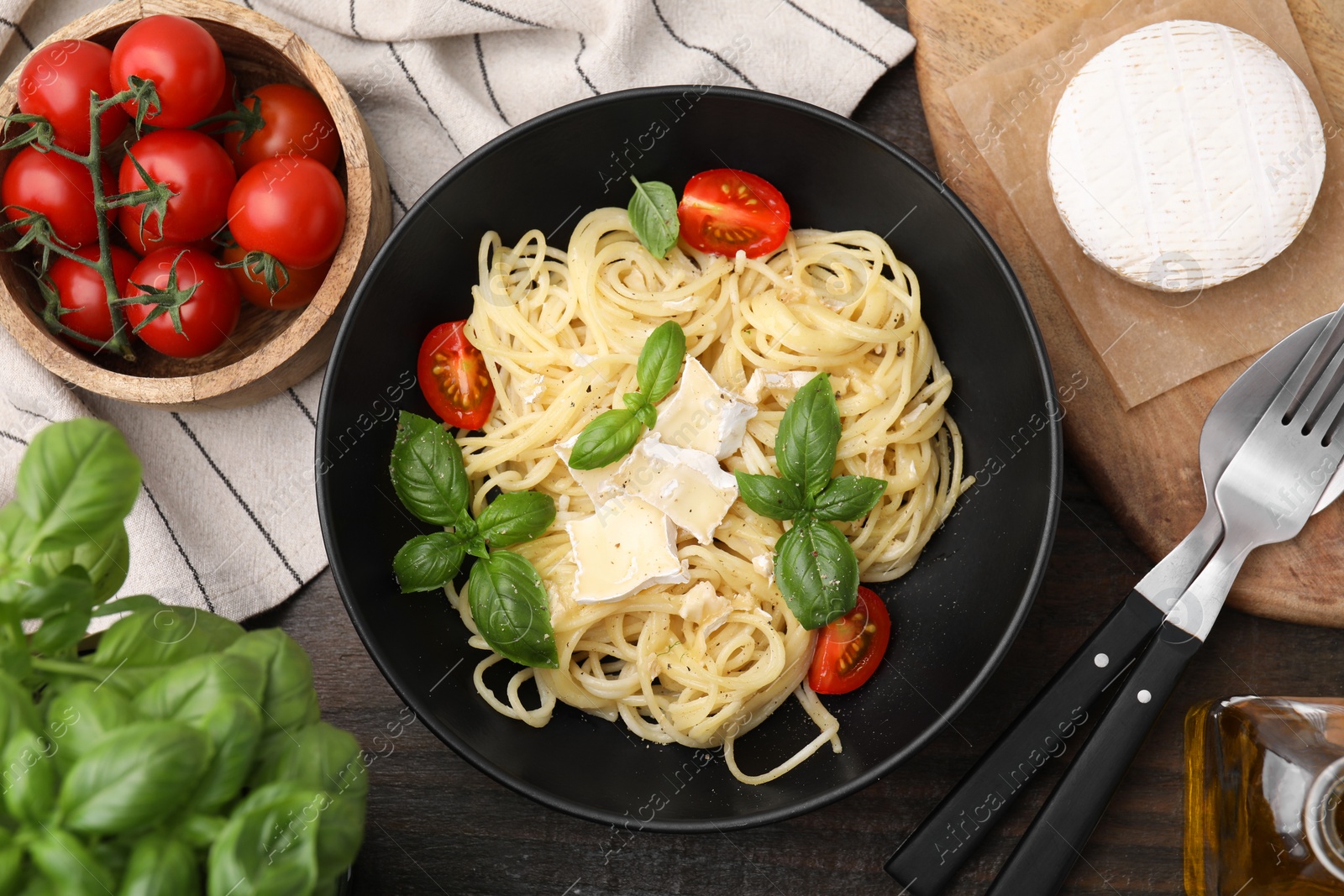 Photo of Delicious pasta with brie cheese, tomatoes and basil leaves served on wooden table, flat lay