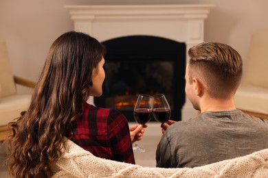 Lovely couple with glasses of wine resting together near fireplace at home