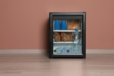 Photo of Mini bar filled with food and drinks near pale pink wall indoors, space for text