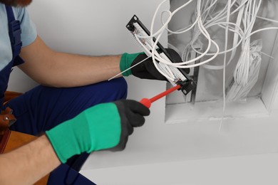 Photo of Electrician with screwdriver fixing patch panel indoors, closeup