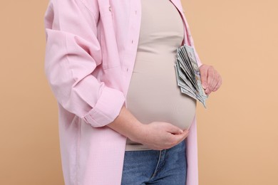 Surrogate mother. Pregnant woman with dollar banknotes on beige background, closeup