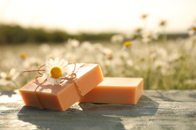 Photo of Chamomile soap bars on blue wooden table in field