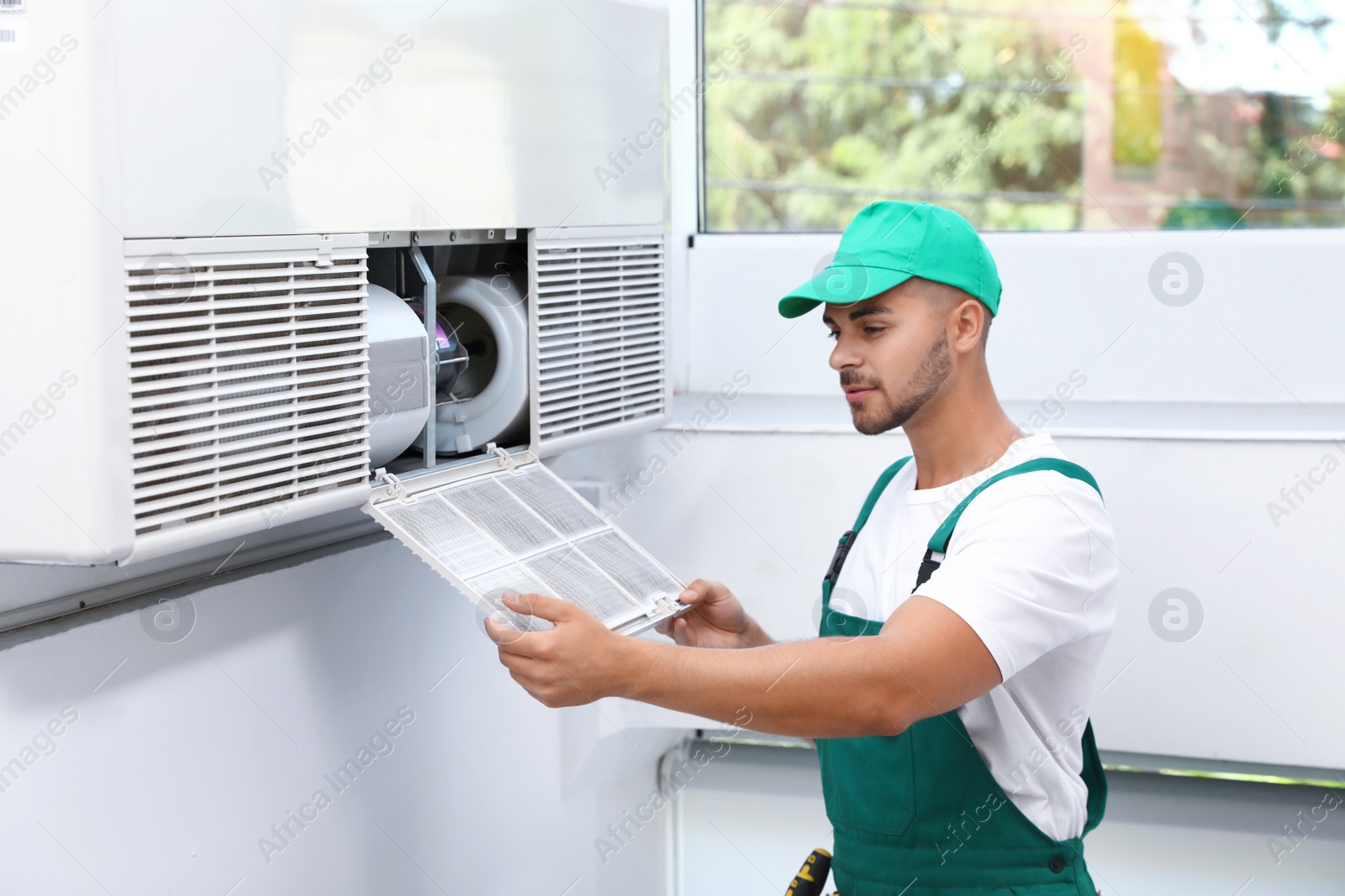 Photo of Professional technician maintaining modern air conditioner indoors