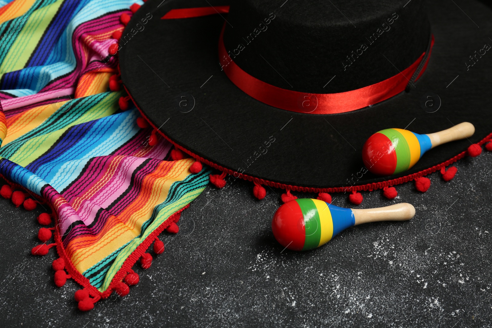 Photo of Mexican sombrero hat, maracas and colorful poncho on grey textured background