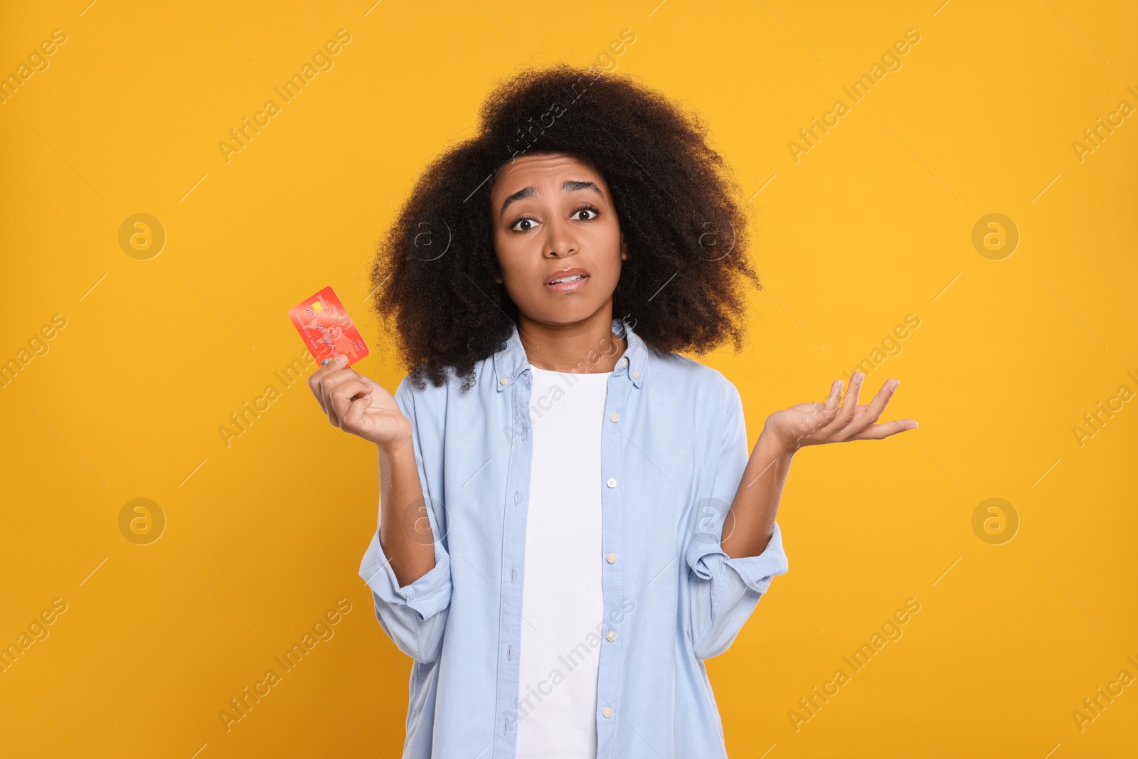 Photo of Confused woman with credit card on orange background. Debt problem