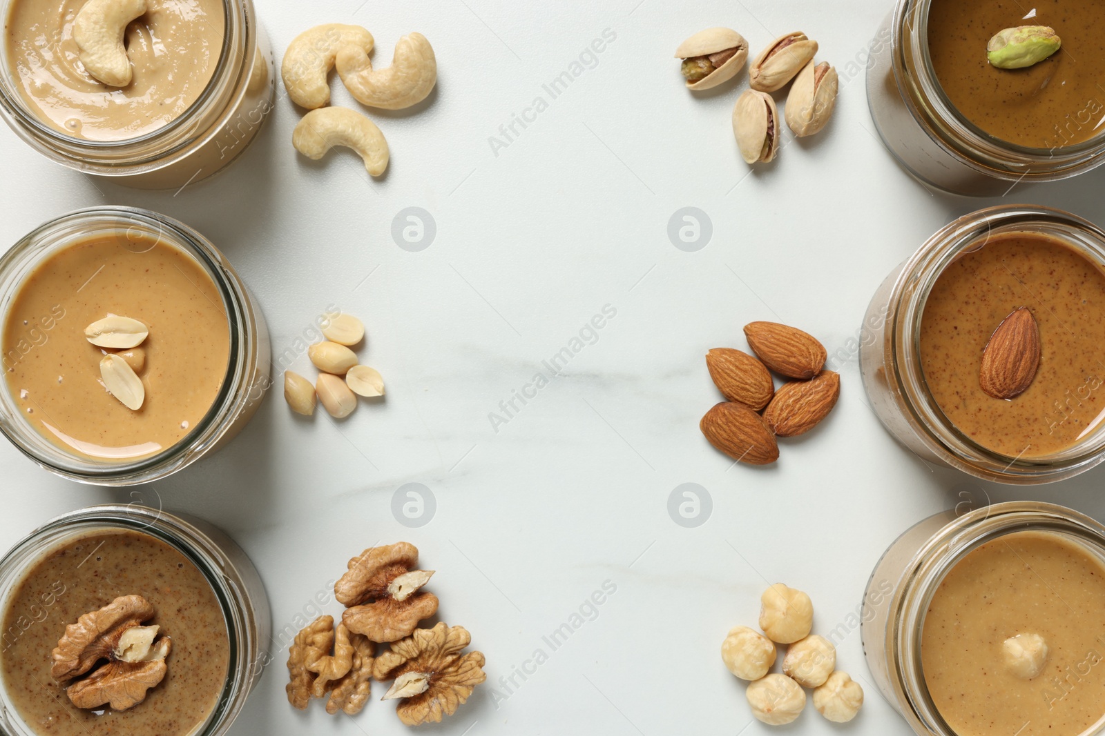 Photo of Tasty nut butters in jars and raw nuts on white marble table, flat lay