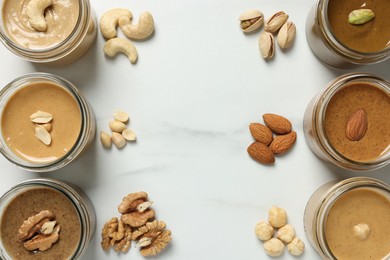 Tasty nut butters in jars and raw nuts on white marble table, flat lay