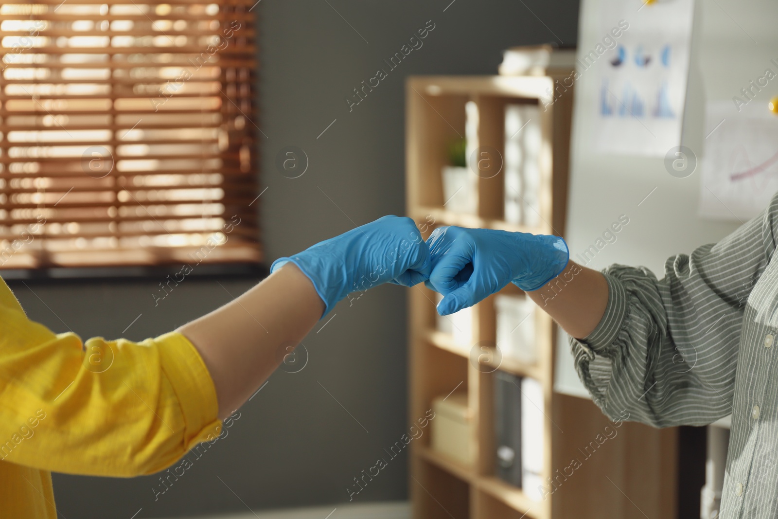 Photo of People greeting each other by bumping fists instead of handshake indoors, closeup