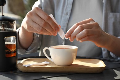 Woman adding sugar into cup of tea at black wooden table in outdoor cafe, closeup