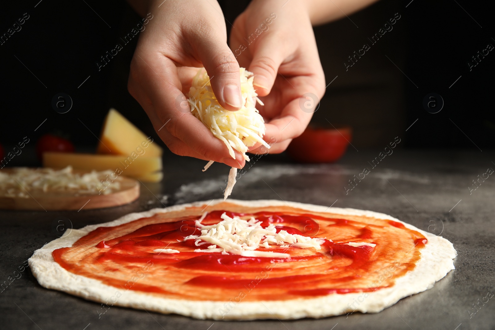 Photo of Woman adding cheese to pizza at grey table, closeup