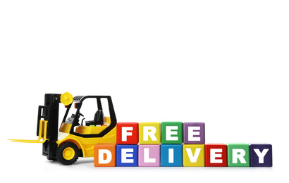 Photo of Toy forklift and cubes with words FREE DELIVERY isolated on white. Logistics and wholesale concept