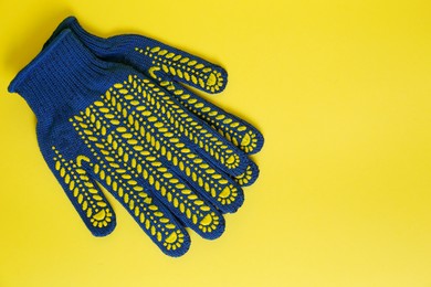 Gardening gloves on yellow background, top view. Space for text