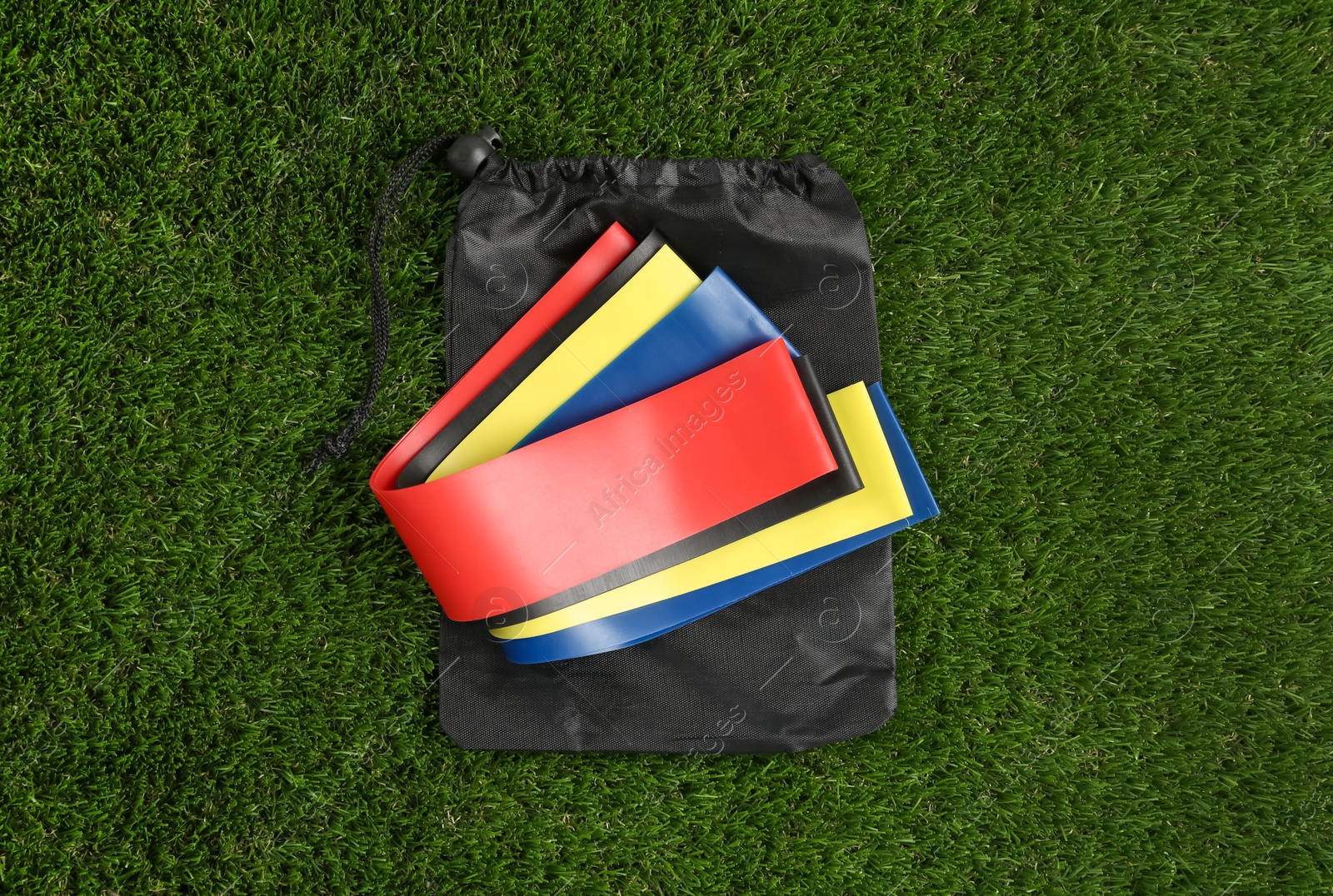 Photo of Bag with fitness elastic bands on green grass, top view