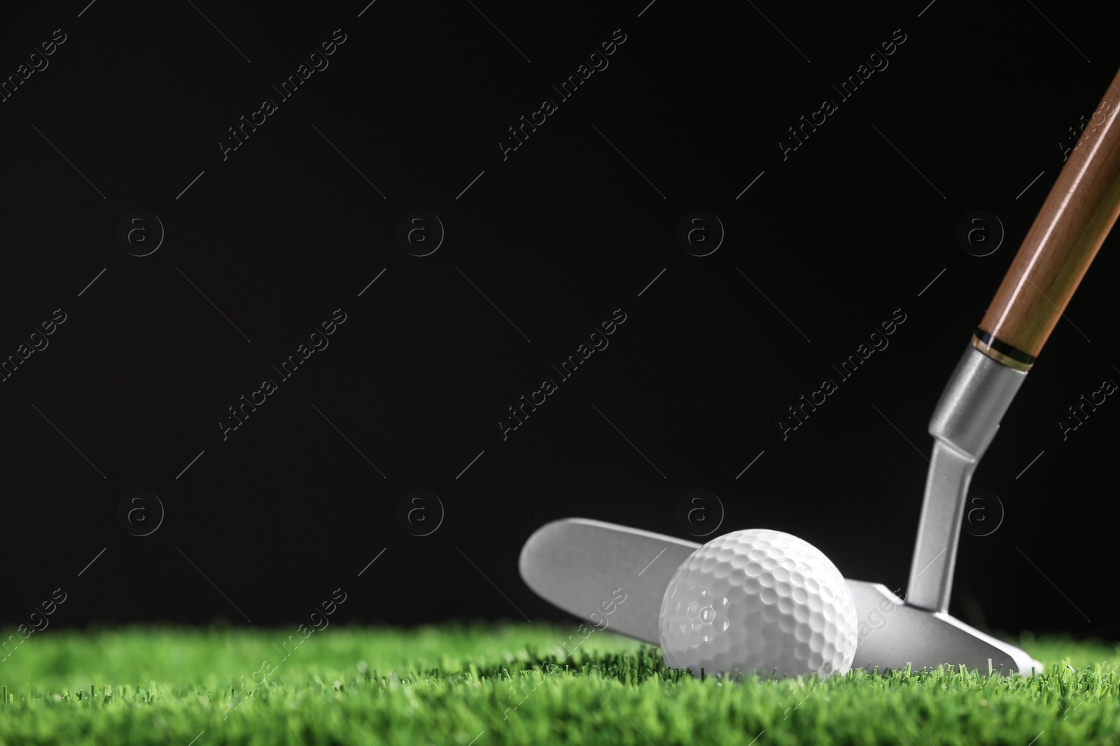 Photo of Hitting golf ball with club on artificial grass against black background, space for text