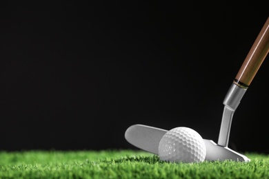 Hitting golf ball with club on artificial grass against black background, space for text