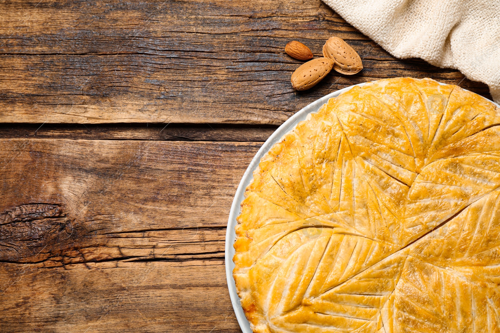 Photo of Traditional galette des rois and almonds on wooden table, flat lay. Space for text