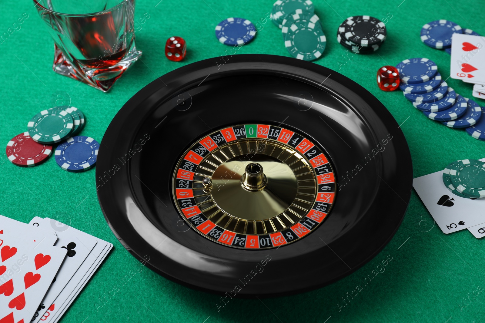 Photo of Roulette wheel, playing cards, chips and dice on green table, closeup. Casino game