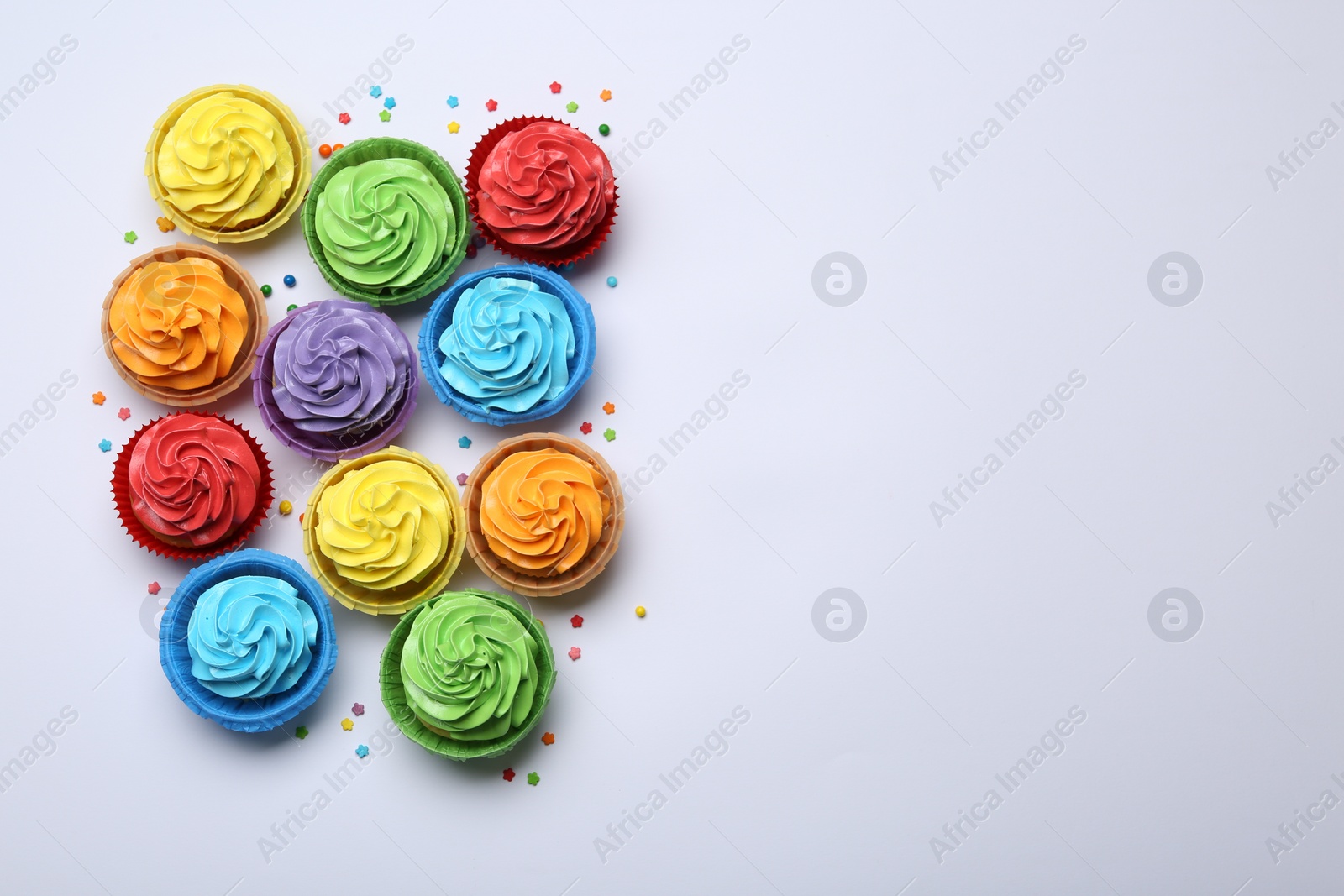 Photo of Many tasty cupcakes with bright cream and sprinkles on white background, flat lay. Space for text