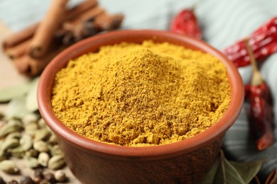 Photo of Curry powder in bowl and other spices on table, closeup