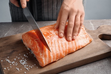 Photo of Woman cutting raw salmon fillet on wooden board