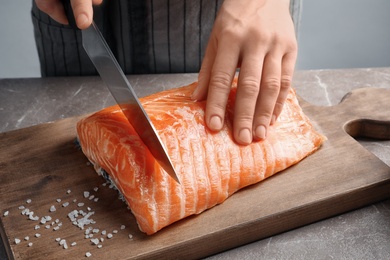 Woman cutting raw salmon fillet on wooden board