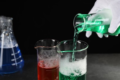 Photo of Scientist working with laboratory glassware at black table, closeup. Chemical reaction