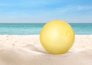Yellow beach ball on sandy coast near sea