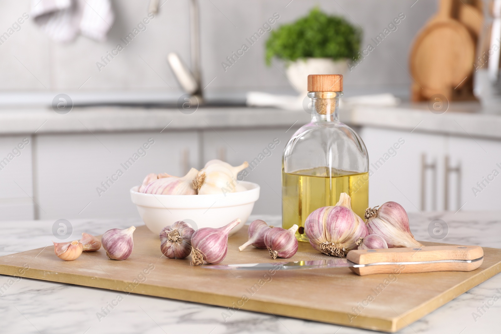 Photo of Fresh raw garlic, knife and oil on white marble table