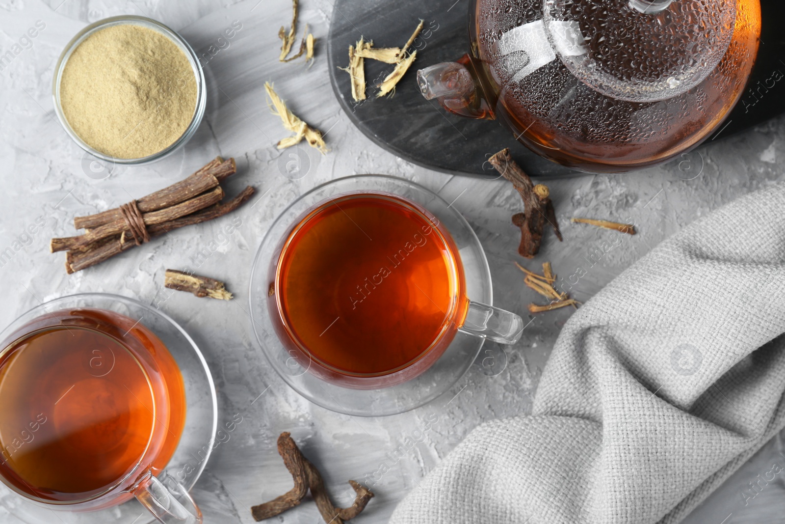 Photo of Aromatic licorice tea, dried sticks of licorice root and powder on light gray textured table, flat lay