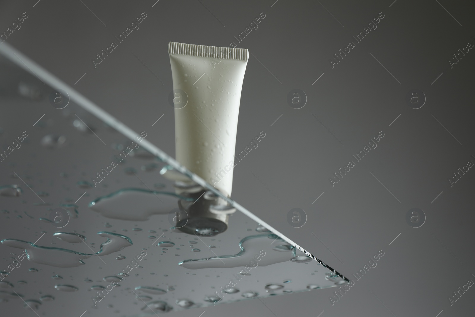 Photo of Tube with moisturizing cream on glass against grey background, low angle view. Space for text