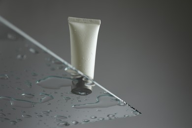 Tube with moisturizing cream on glass against grey background, low angle view. Space for text