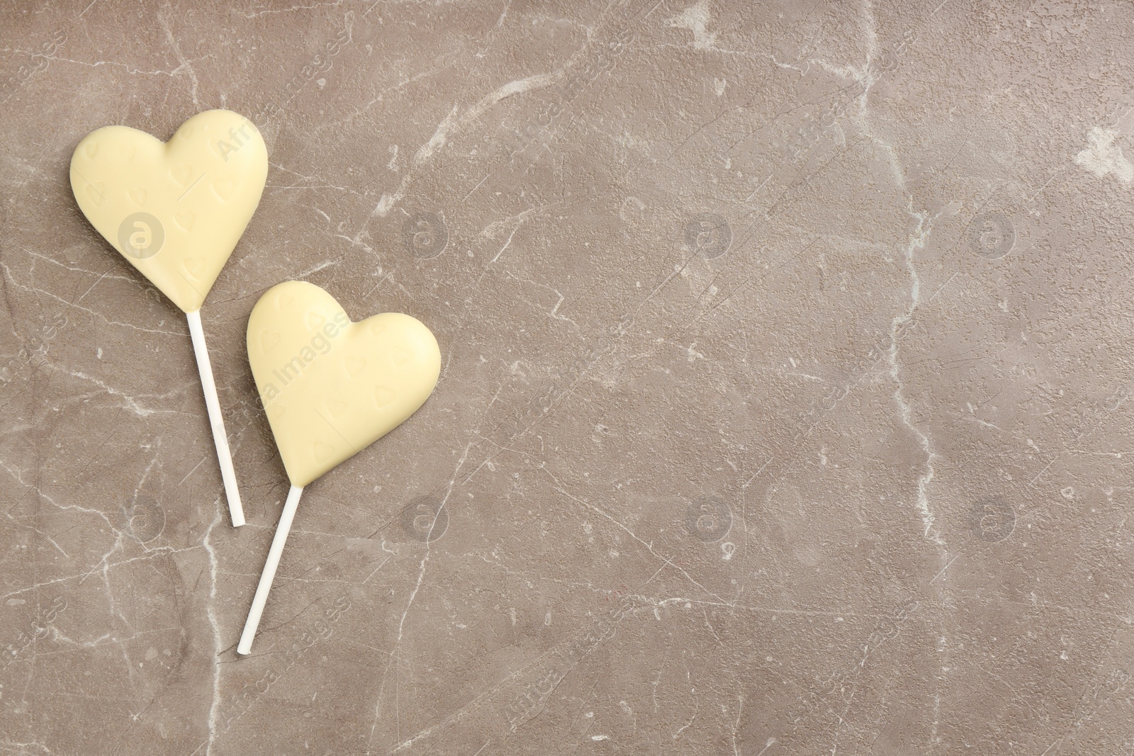 Photo of Chocolate heart shaped lollipops on light grey marble table, flat lay. Space for text