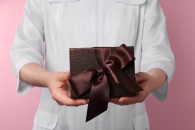 Photo of Doctor holding gift box on pink background, closeup. Medical present