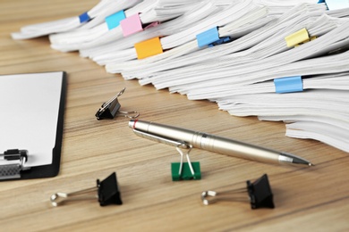 Photo of Stack of documents with binder clips, clipboard and pen on wooden table, closeup view