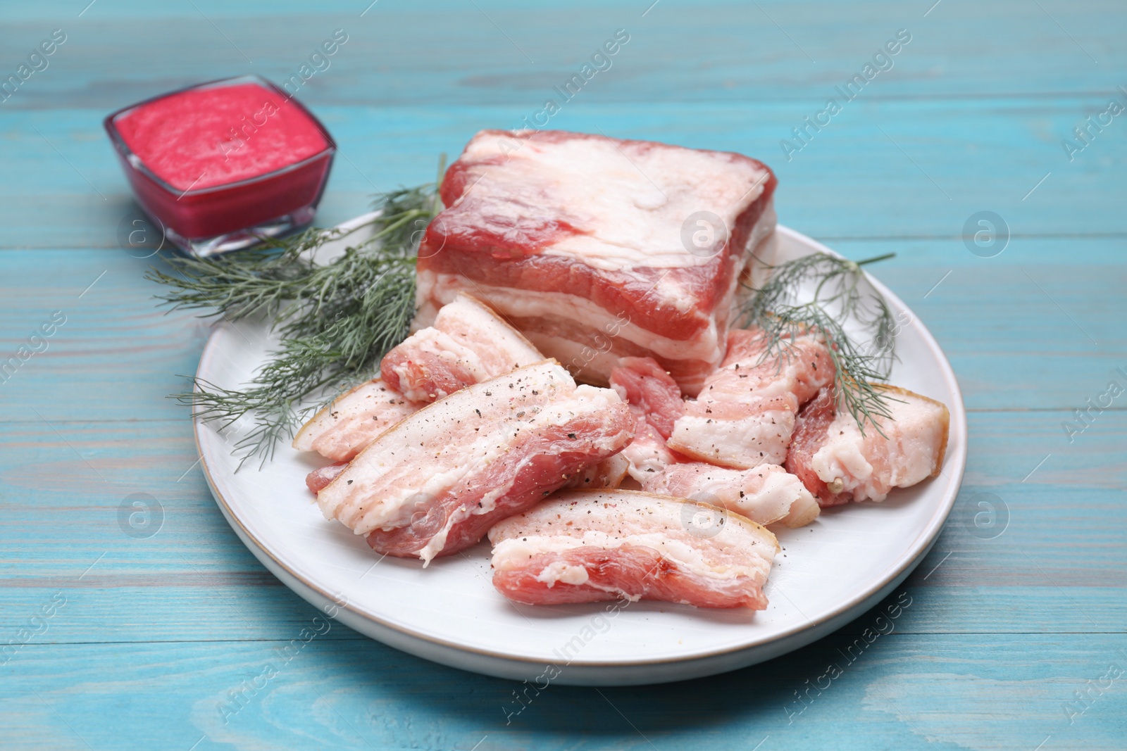 Photo of Pieces of pork fatback with dill and sauce on light blue wooden table