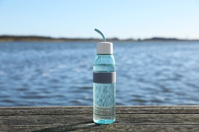 Photo of Glass bottle with water on wooden pier near river outdoors