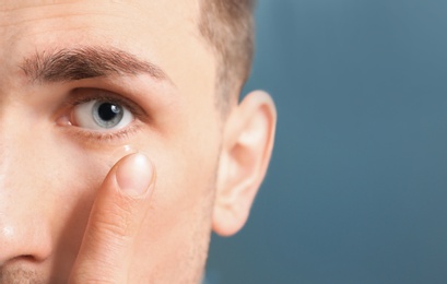 Photo of Young man putting contact lens in his eye on color background