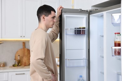 Photo of Upset man near empty refrigerator in kitchen